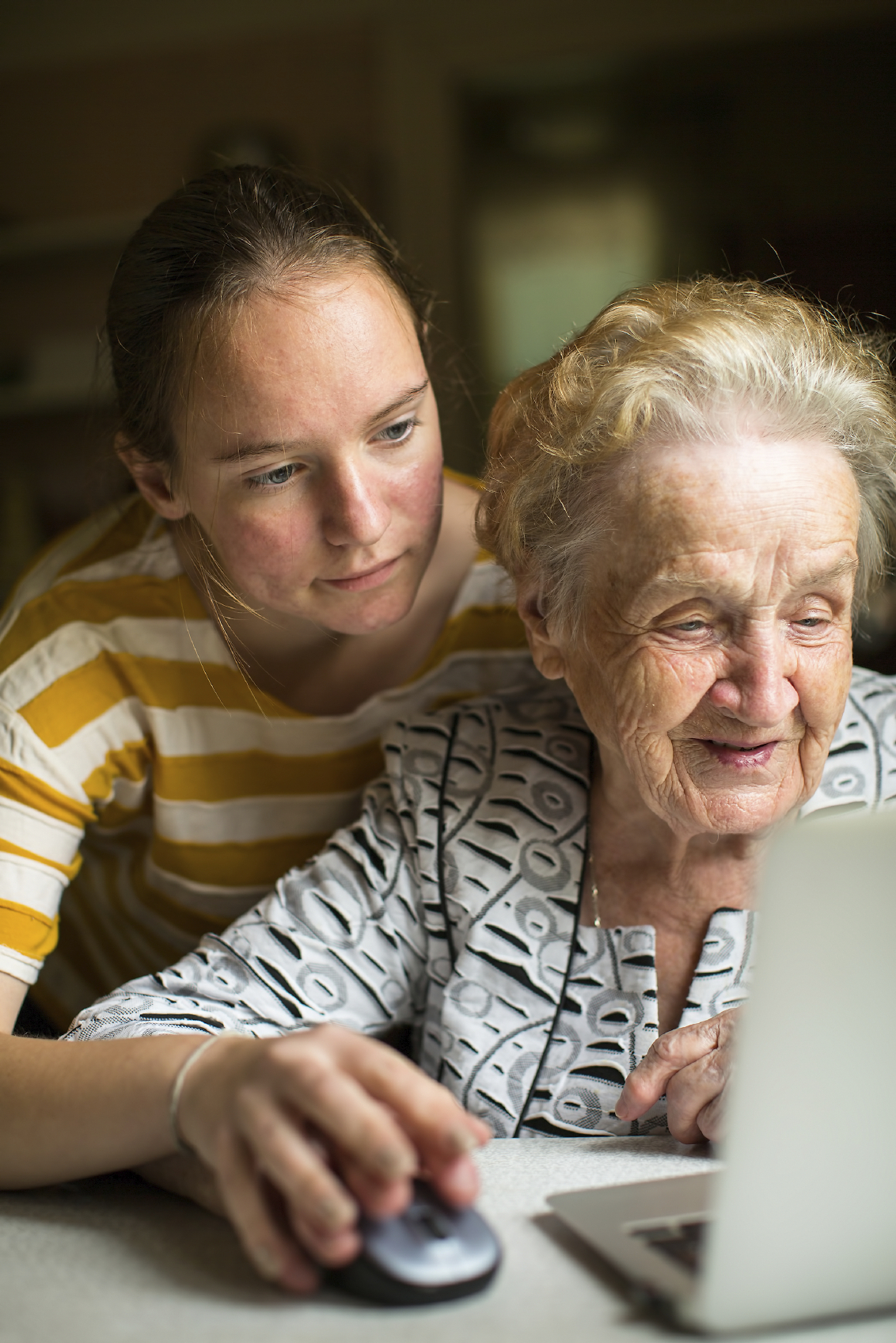 Young girl teaches elderly woman working on the computer. Granddaughter with her grandmother near the computer.